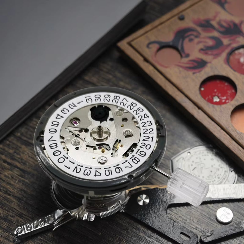 Close-up of a vintage-style mechanical watch movement or pocket watch component with visible gears, a white dial, and a transparent cover, placed on a dark wooden surface with a decorative box in the background.