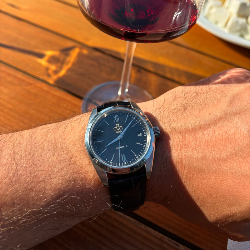 Wrist wearing a watch with a glass of red wine and snacks on a wooden table