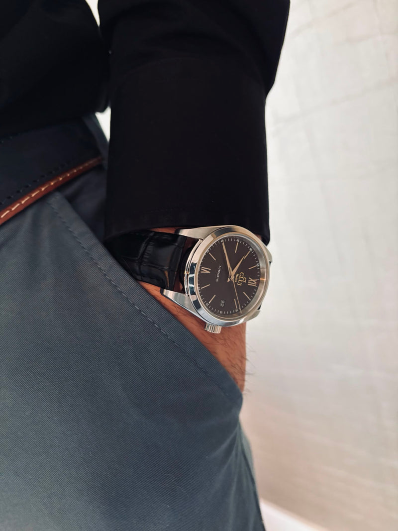 Close-up of a wrist wearing a watch with a black strap and brown leather case, against a neutral background.